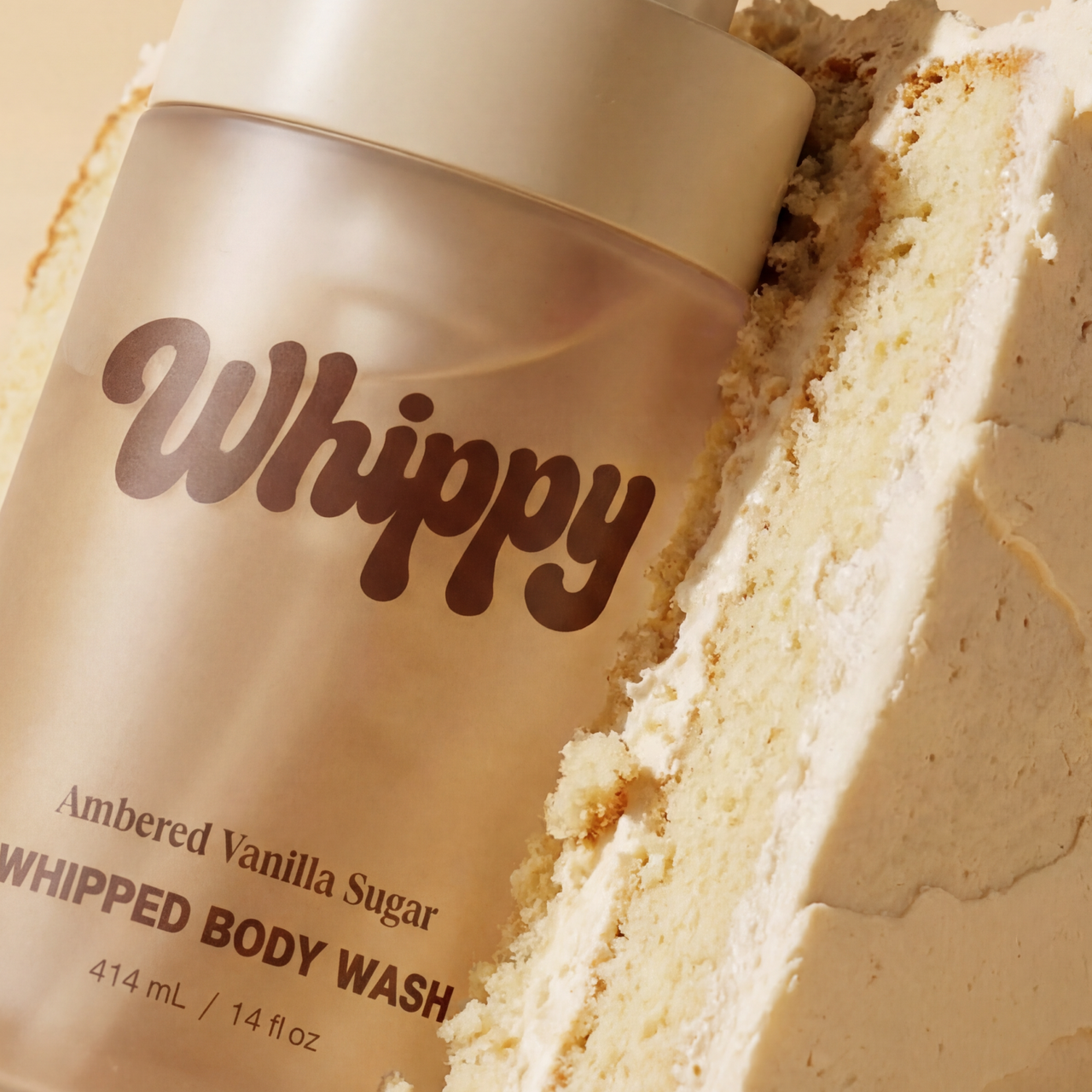 Whippy Ambered Vanilla Sugar Whipped Body Wash bottle resting against a slice of vanilla cake